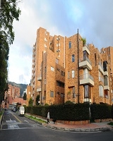 Imagen de una vía y centrado un edificio de varios pisos, el cual es rodeado por zona verde y árboles. 