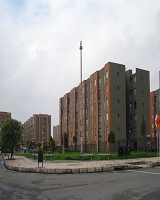 Imagen de conjunto residencial con bloques de apartamentos, rodeado de zona verde y vías vehículares. 