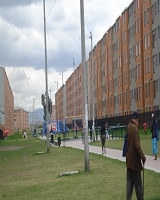 Imagen del costado de un conjunto residencial de apartamentos y a su izquierda una zoma verde que la atraviesa un camino peatonla
