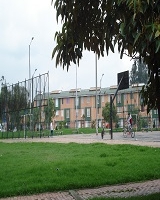 Imagen que contiene en su parte frontal una zona verde con caminos peatonales y un parque con canchas de juegos, al fondo se encuentra un conjunto residencial de apartamentos. 