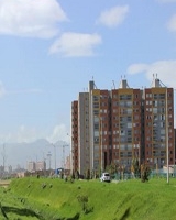 La imagen presenta un paisaje con zona verde y al fondo se observa un conjunto residencial de apartamentos