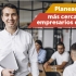 Hombre con portatil en sus manos, al fondo mujeres y hombres reunidos en mesa de trabajo.