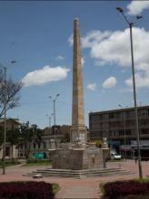 Columna en piedra terminada en punta, sobre un basamento, con una altura aproximada de 6 pisos, localizada en el centro de la Plazoleta de Los Mártires, frente a la Basílica del Voto Nacional