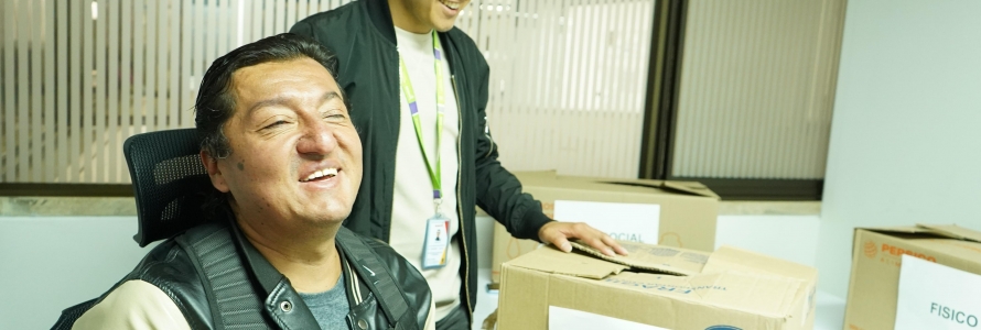 Hombre con discapacidad visual, sentado dentro de una sala, ejerciendo el derecho al voto a través de un tarjetón en braile, para elegir representantes distritales de discapacidad.