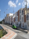 Imagen en la se ve una vía vehicular que separa una zona verde y un conjunto de casas.  